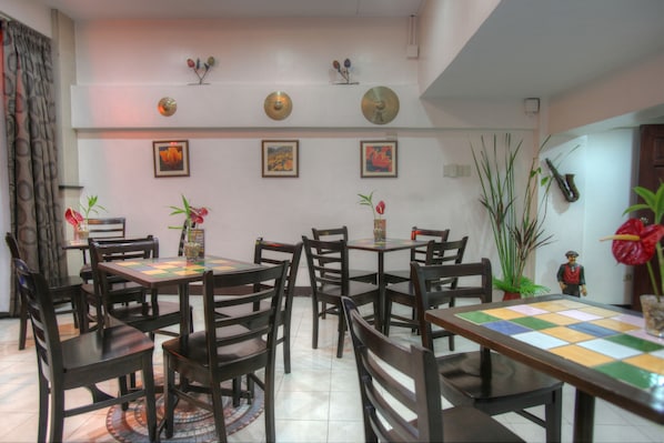 Un comedor con varias mesas y sillas, suelo de baldosas y decoraciones en las paredes, incluyendo cuadros y elementos montados.