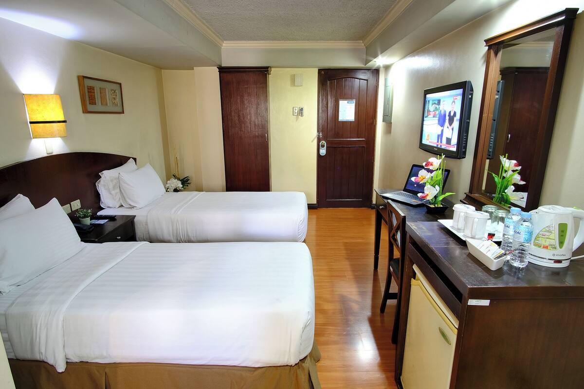 A hotel room with two beds, a desk with a laptop, a coffee maker, and a mirror.