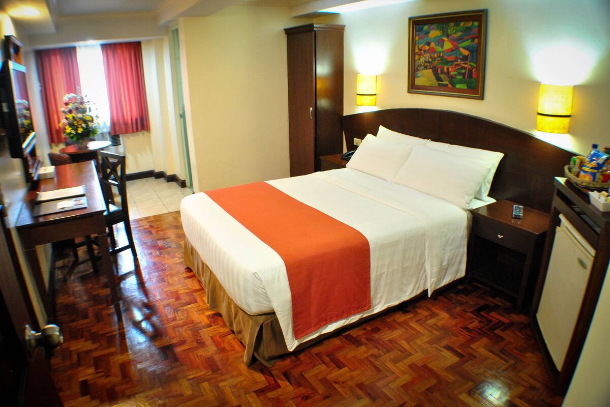 A hotel room with a bed, bedside table, lamp, and a desk with a chair.