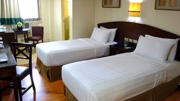 A hotel room with two beds, a desk, a chair, and a small table.