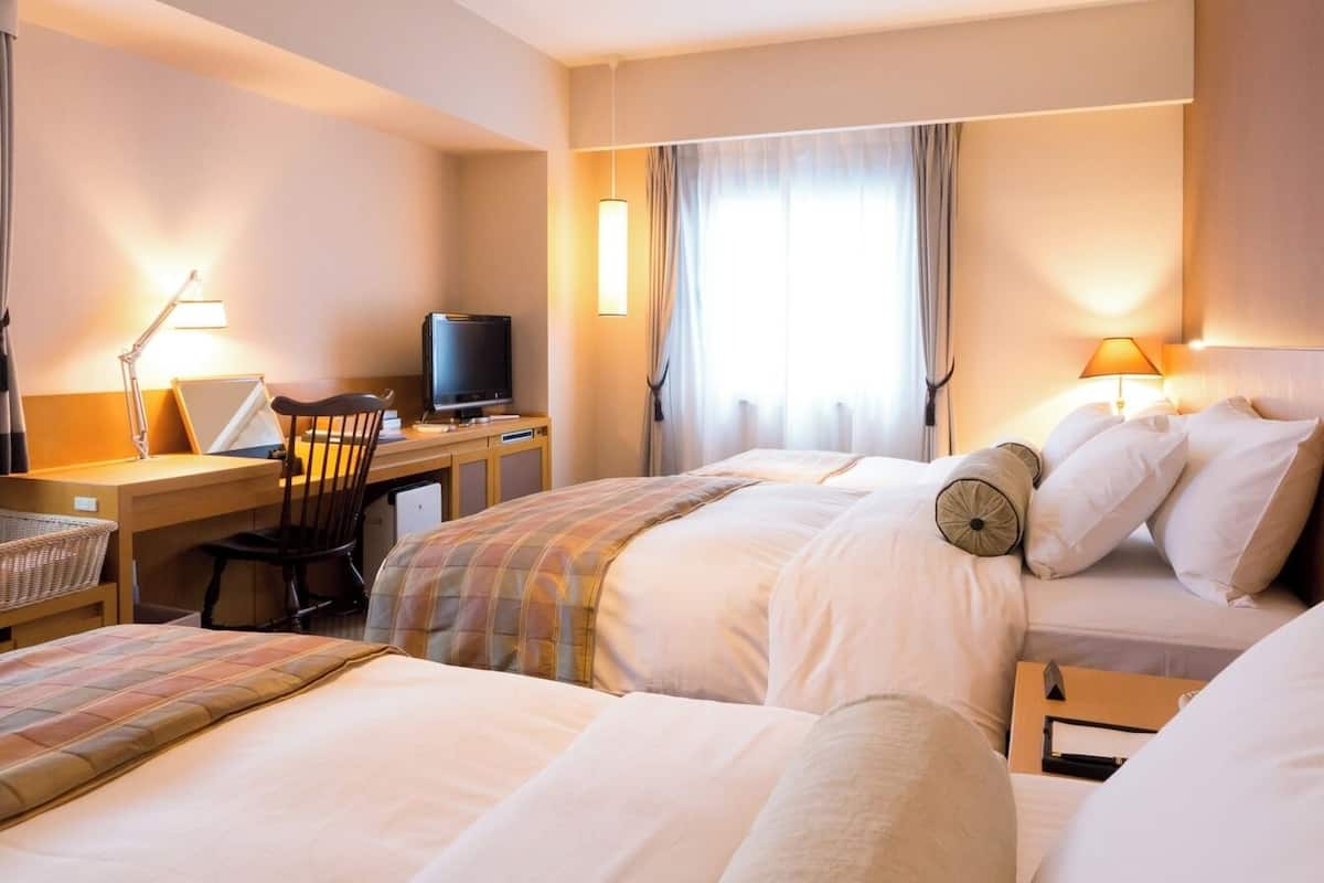 Une chambre d’hôtel avec deux lits, un bureau avec un ordinateur, une chaise et un téléviseur.