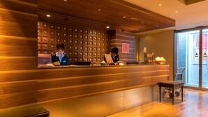 A reception desk with a wooden panel design, a seating area, and a view of the outside through large windows. - Matsumoto Marunouchi Hotel (Matsumoto)
