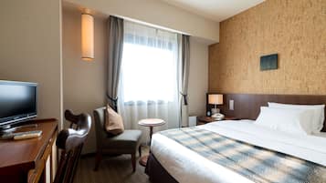 A hotel room with a bed, a desk with a TV, a chair, a small table, and a window with curtains.