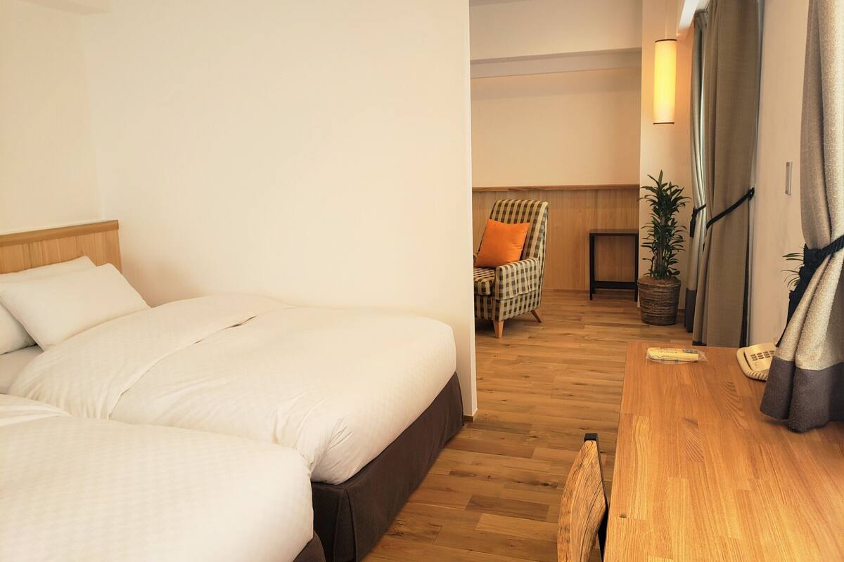 A hotel room with a double bed, a wooden desk, a chair, and a potted plant.