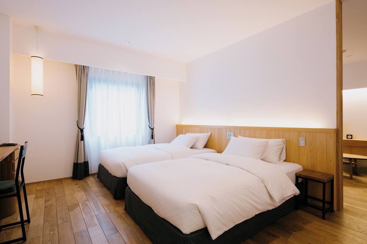 Une chambre d’hôtel avec deux lits, un bureau et une chaise.