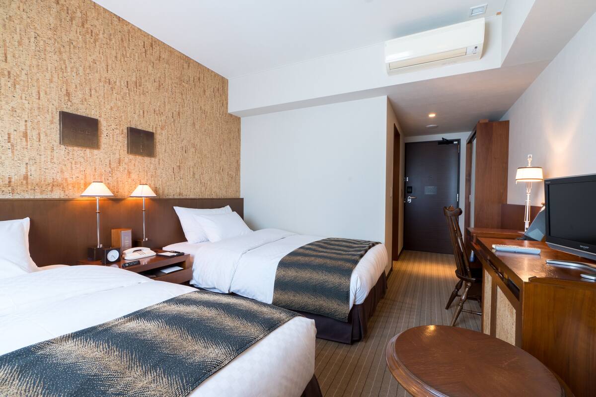 A hotel room with two beds, a desk, a chair, a TV, and a wooden accent wall.
