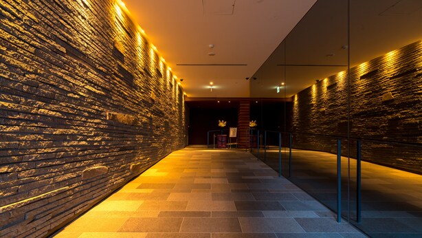 A corridor with a brick wall on one side and a glass partition on the other, illuminated by warm lighting. - Matsumoto Marunouchi Hotel (Matsumoto)