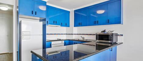 Eine moderne Küche mit blauen Schränken, einem weißen Kühlschrank, einer Mikrowelle und einer Arbeitsplatte aus Granit.