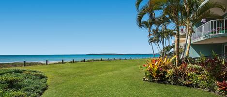 A well-maintained lawn with a view of the ocean and a building with balconies overlooking the beach.