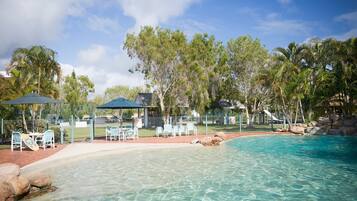 A clear pool with lounge chairs and umbrellas, surrounded by trees and a gazebo.