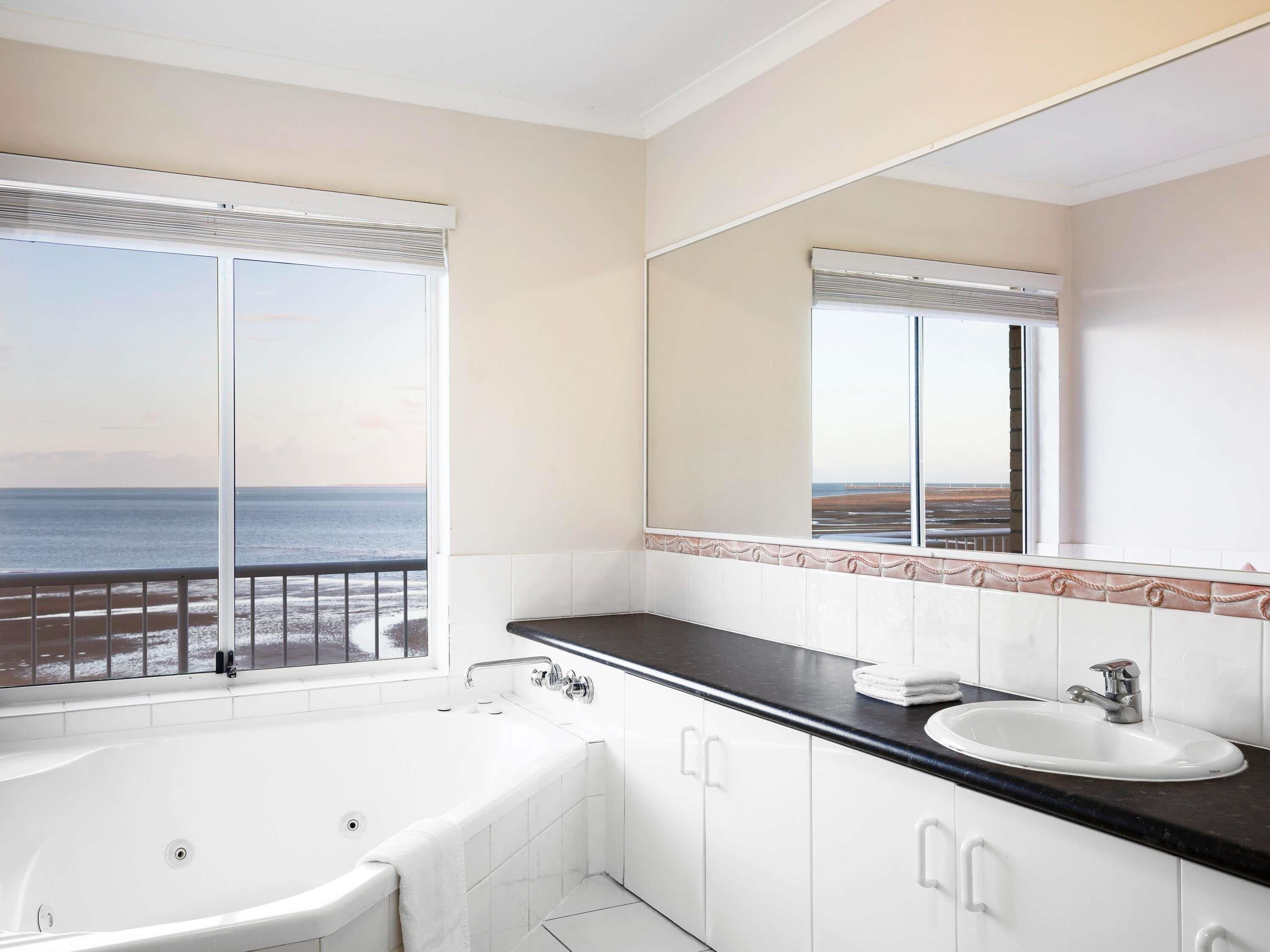 Une salle de bain avec une baignoire, un lavabo, un grand miroir et une vue sur la mer.