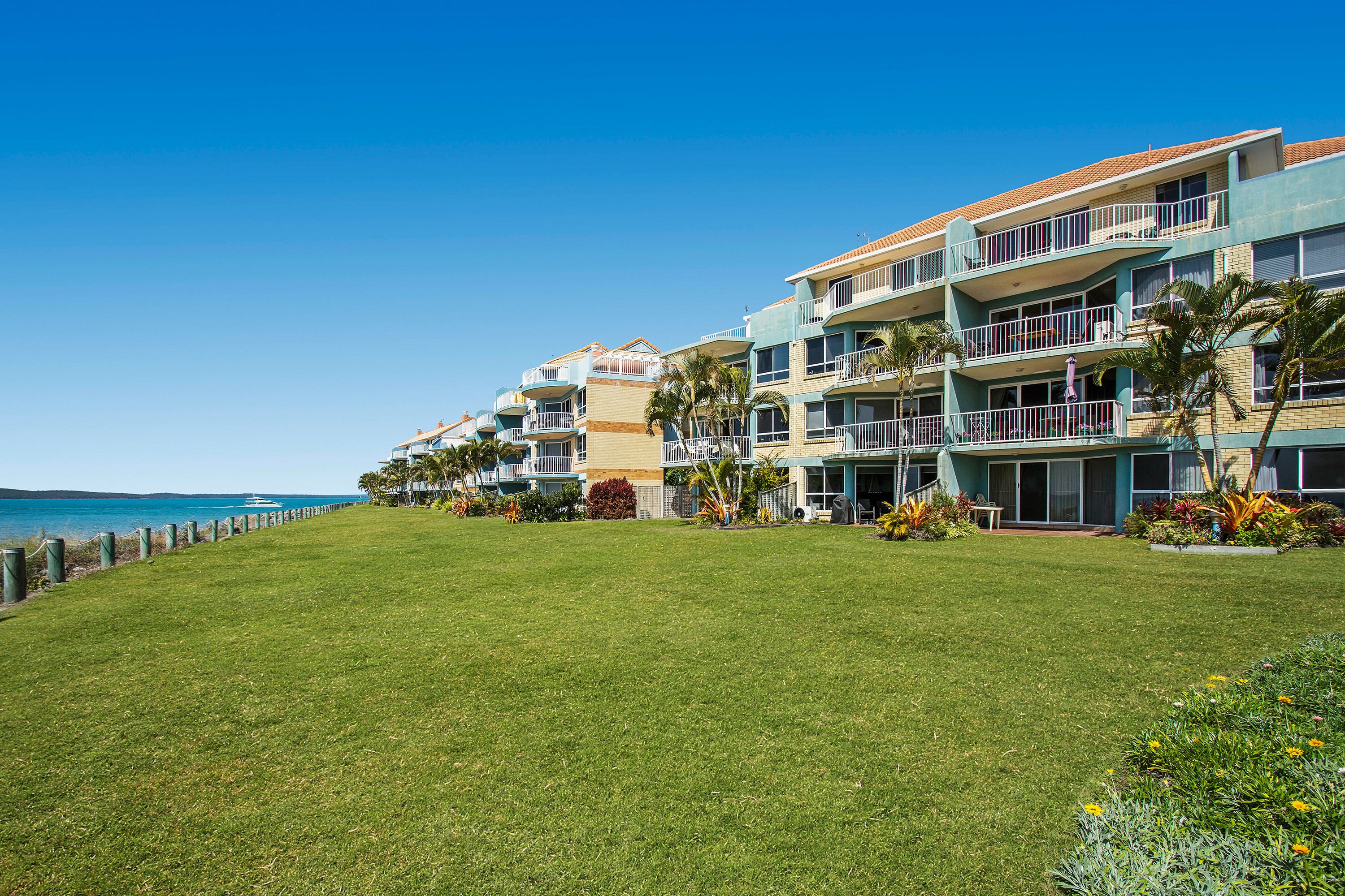 Un hôtel situé en bord de mer, doté de nombreux balcons, d’une pelouse verdoyante et offrant une vue sur l’océan.