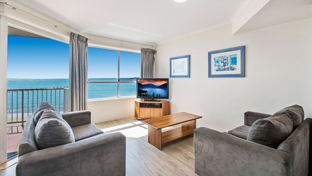 Una sala de estar moderna con un amplio ventanal con vista al mar, una mesa de centro de madera y dos sofás grises.