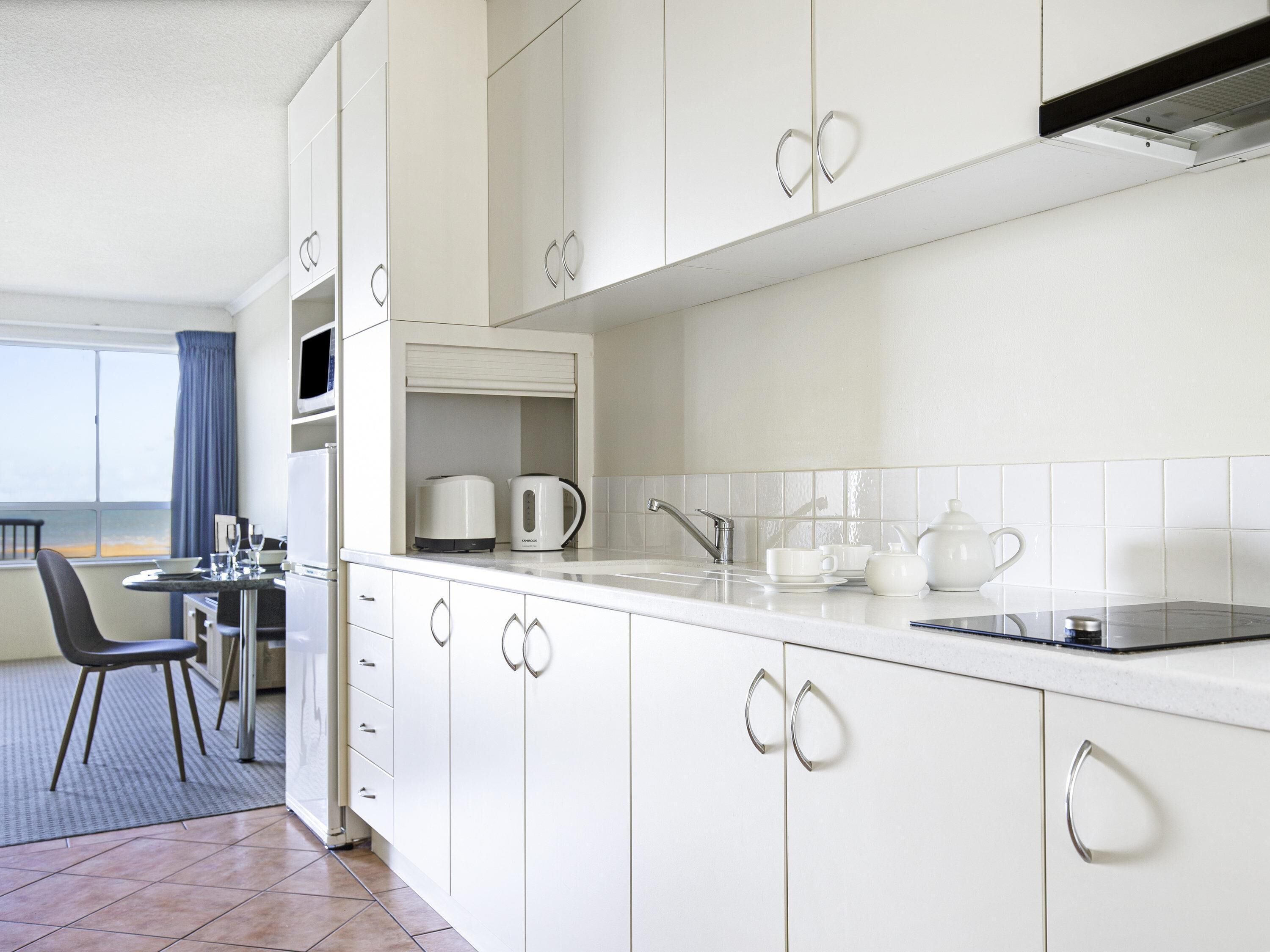 A modern kitchen with white cabinets, a dining area with a table and chairs, and a view of the sea through a window.
