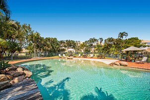 Una piscina cristalina rodeada de sillas de descanso y palmeras, con una terraza de madera y una valla que delimita el espacio.