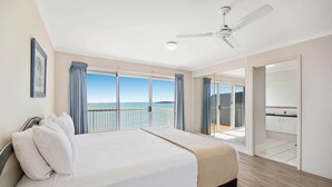 Un dormitorio con una cama grande, un ventilador de techo y vista al mar desde las puertas del balcón.