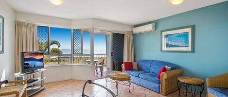 Una sala de estar con televisor, muebles de mimbre, un sofá azul y vista al océano.