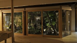 Un interior moderno con amplios ventanales correderos que dan a un jardín con fuente de agua y plantas tropicales.
