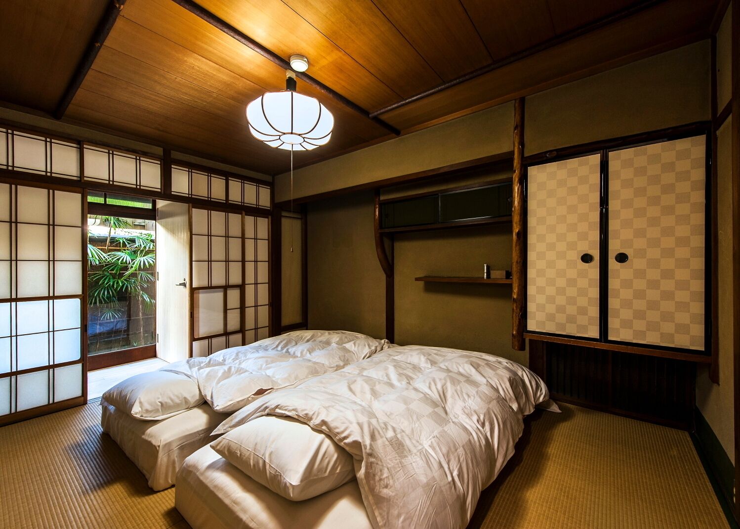 Una habitación de estilo japonés tradicional con suelo de tatami, techo bajo y una cama con ropa blanca.