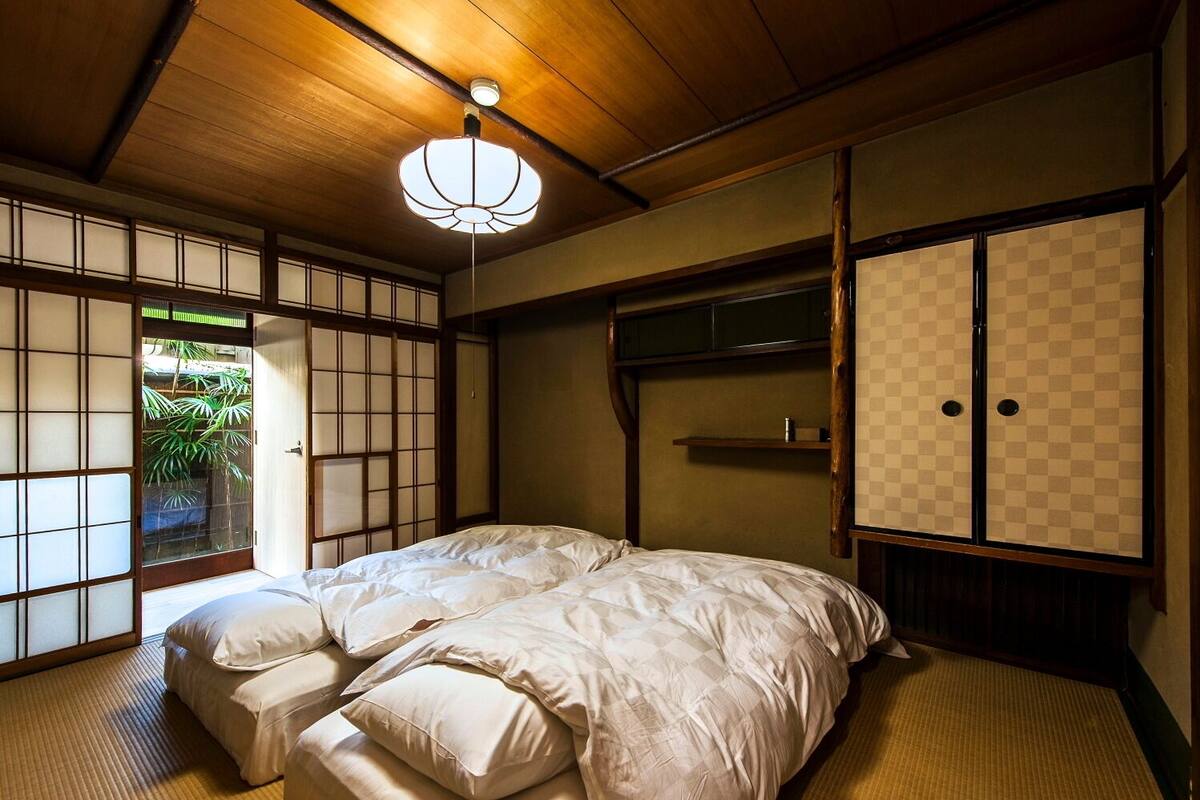A traditional Japanese-style room with tatami flooring, a low ceiling, and a bed with white bedding.
