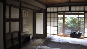 Una habitación tradicional japonesa con suelo de tatami, una cama baja de madera y un divisor corredizo shoji que da a un jardín.