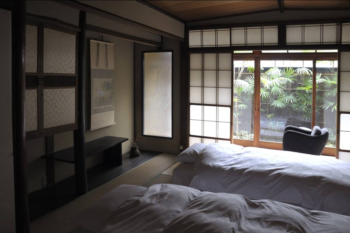 A traditional Japanese-style room with tatami flooring, a low wooden bed, and a sliding shoji screen door leading to a garden.
