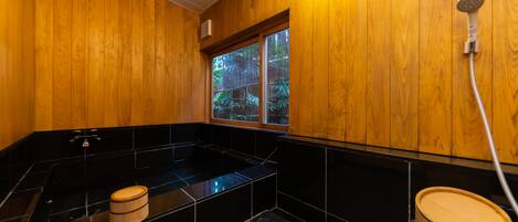 A wooden interior with a black bathtub, a wooden bucket, and a window with a view of greenery.