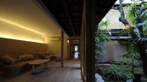 Un interior moderno con suelo de madera, un sofá, una mesa y vistas a un jardín con plantas y un farol de piedra.