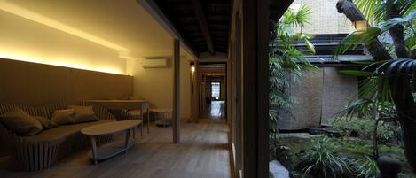 A modern interior with a wooden floor, a sofa, a table, and a view of a garden with plants and a stone lantern.
