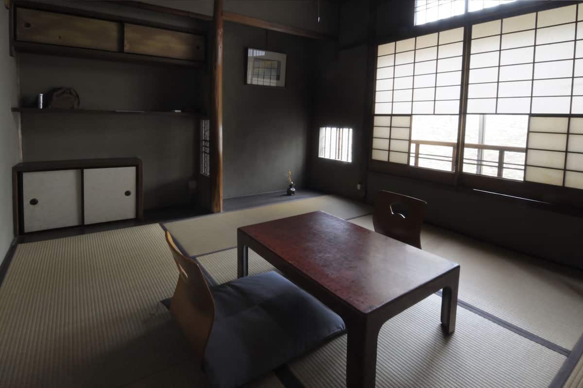 A traditional Japanese room with tatami flooring, a low table, and a chair.