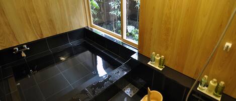 A modern bathroom with a black bathtub, wooden cabinets, and a window with a view of greenery.