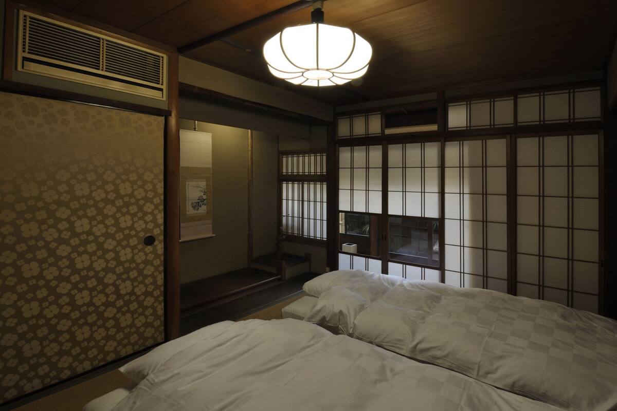 A traditional Japanese-style room with tatami flooring, a shoji screen door, a ceiling fan, and a bed with white bedding.