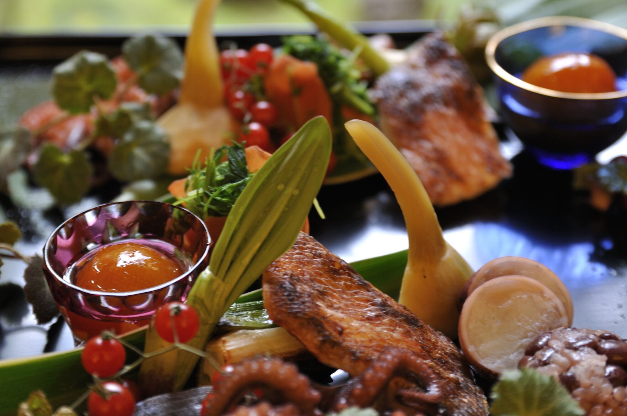 Verschiedene gegrillte Meeresfrüchte und Gemüse, darunter Fisch, Calamari und Kirschtomaten, auf einer Platte angerichtet.