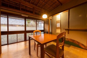 Un comedor con mesa y sillas de madera, ventanas amplias con vidrio esmerilado y un ventilador de techo.