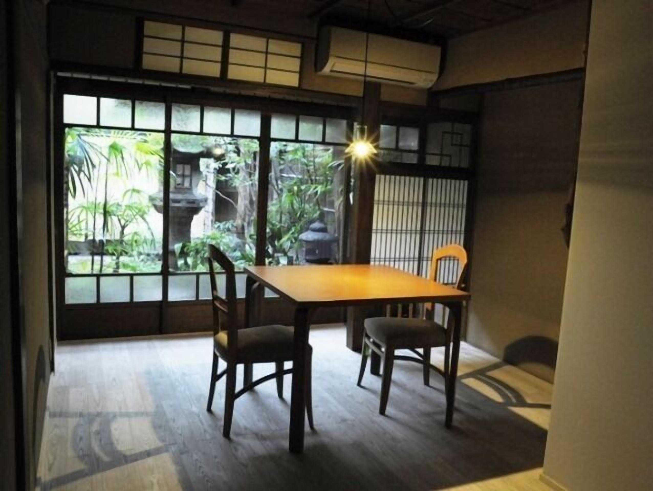Una habitación japonesa tradicional con suelo de tatami, una mesa baja y puertas correderas que dan a vistas de vegetación.