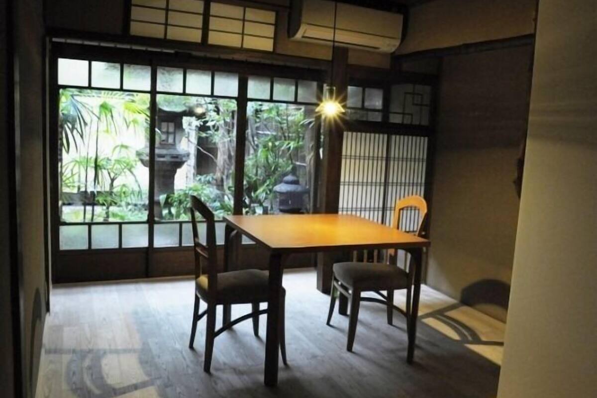 A traditional Japanese room with tatami flooring, a low table, and sliding doors with a view of greenery outside.