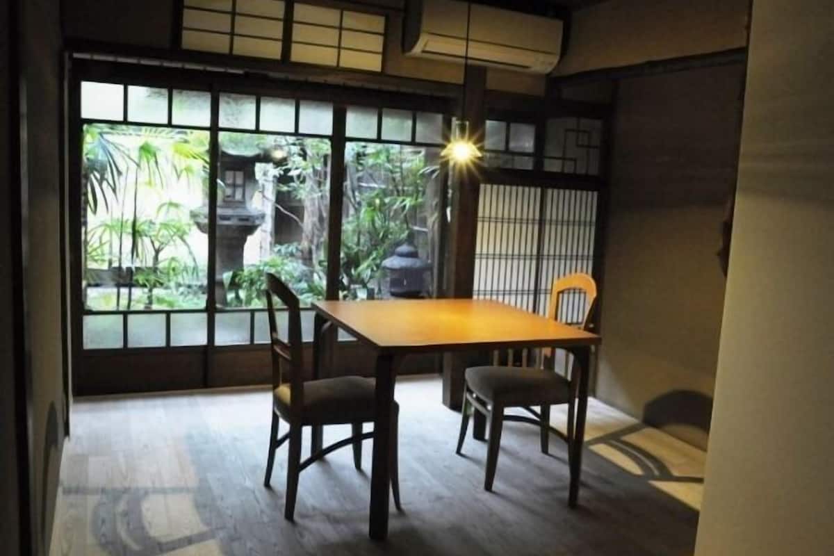 Quarto japonês tradicional com tatames, uma mesa baixa e portas deslizantes com vista para o verde lá fora.