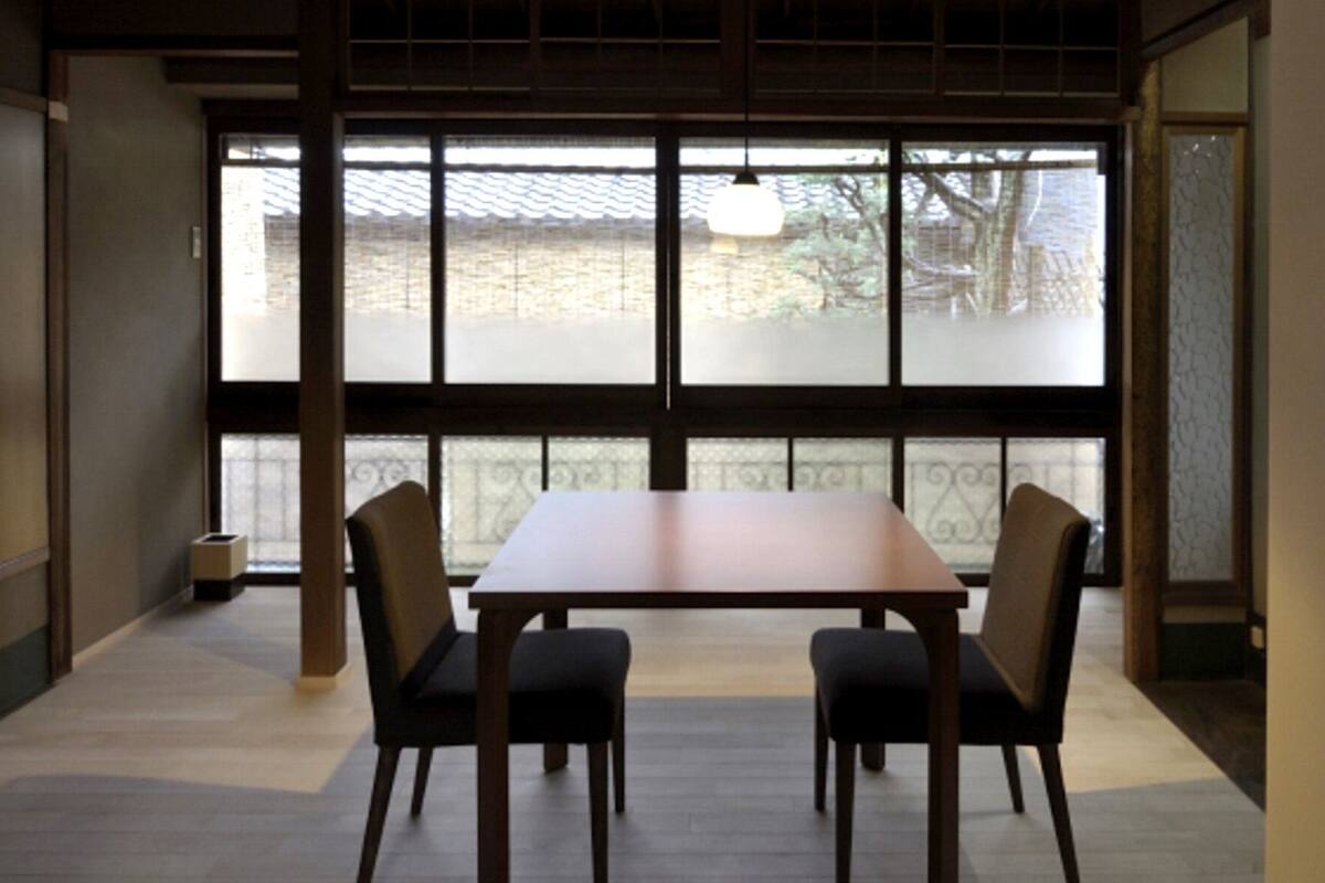 A room with a large window, a wooden table, and four chairs.