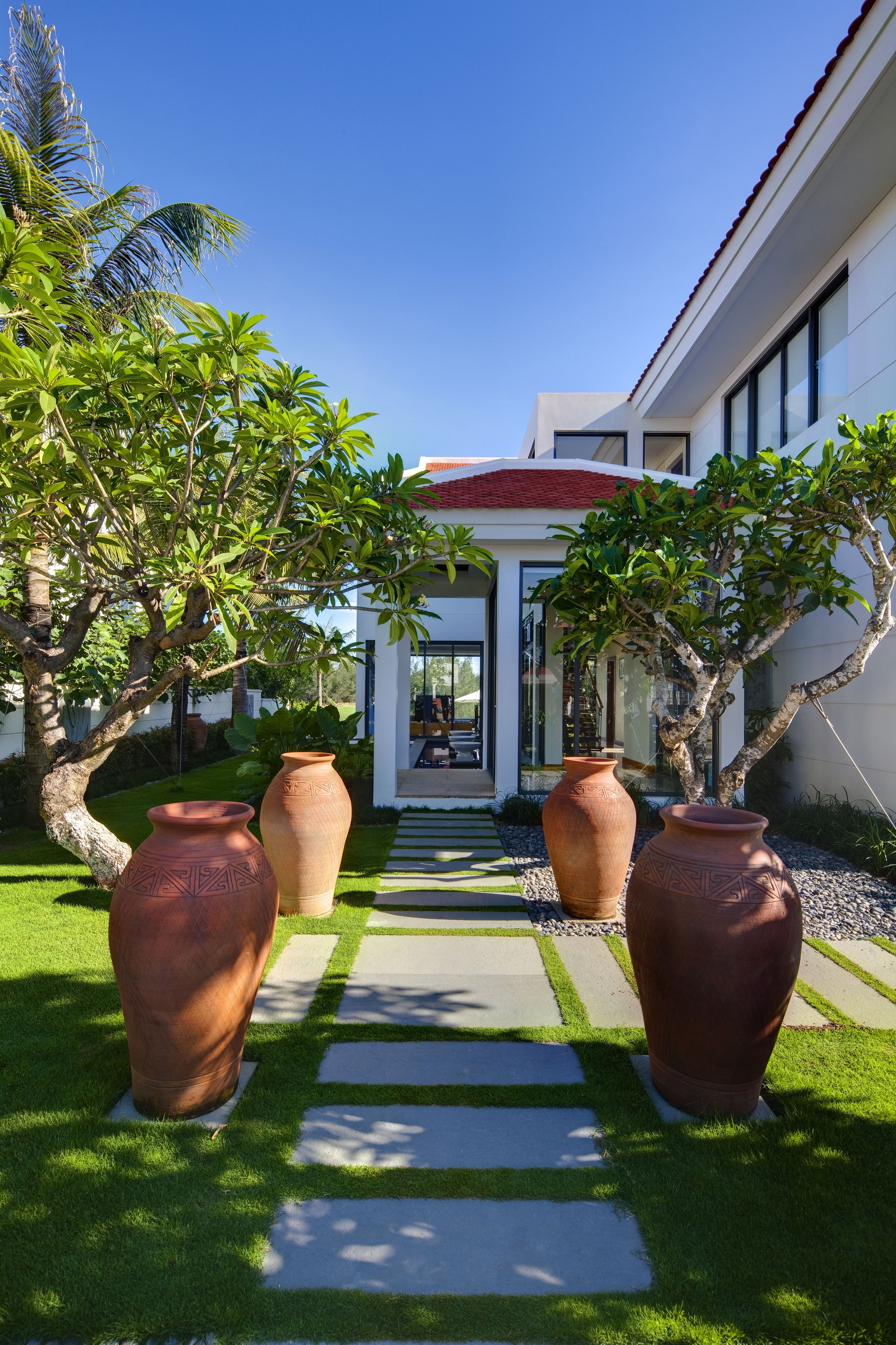 A pathway leading to a modern house with large terracotta pots and lush greenery.