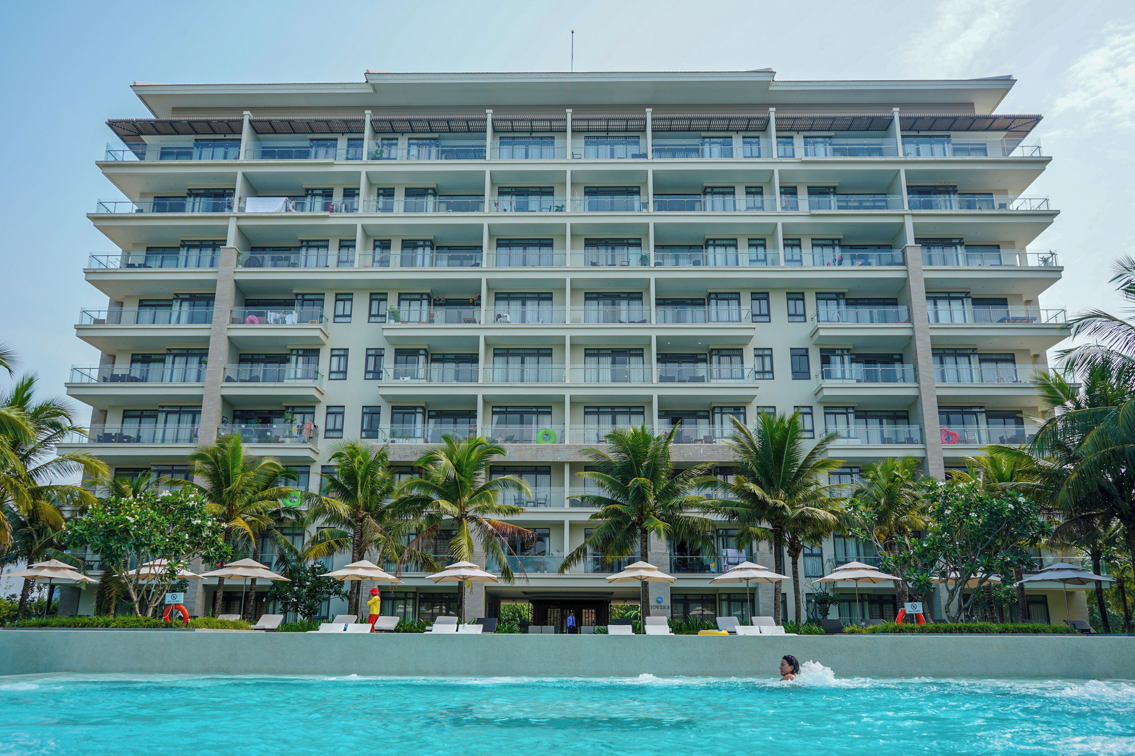 Un hotel de varios pisos con balcones, piscina y palmeras.