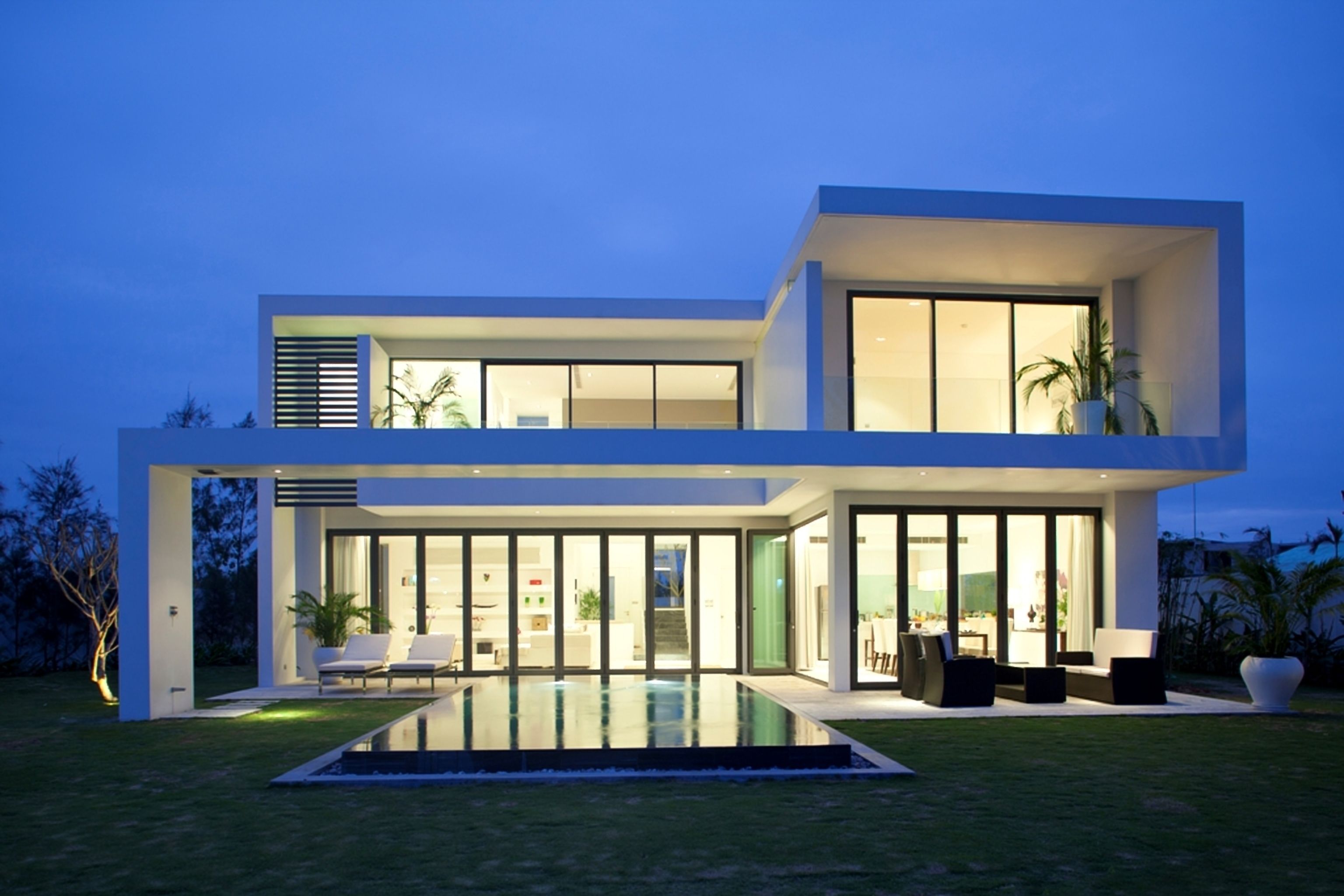 Une maison moderne à deux étages dotée d’une piscine, de grandes fenêtres et d’un espace salon extérieur.