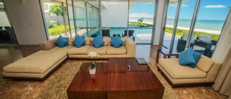 A modern living room with a large sectional sofa, a wooden coffee table, and a view of the ocean through large glass doors.