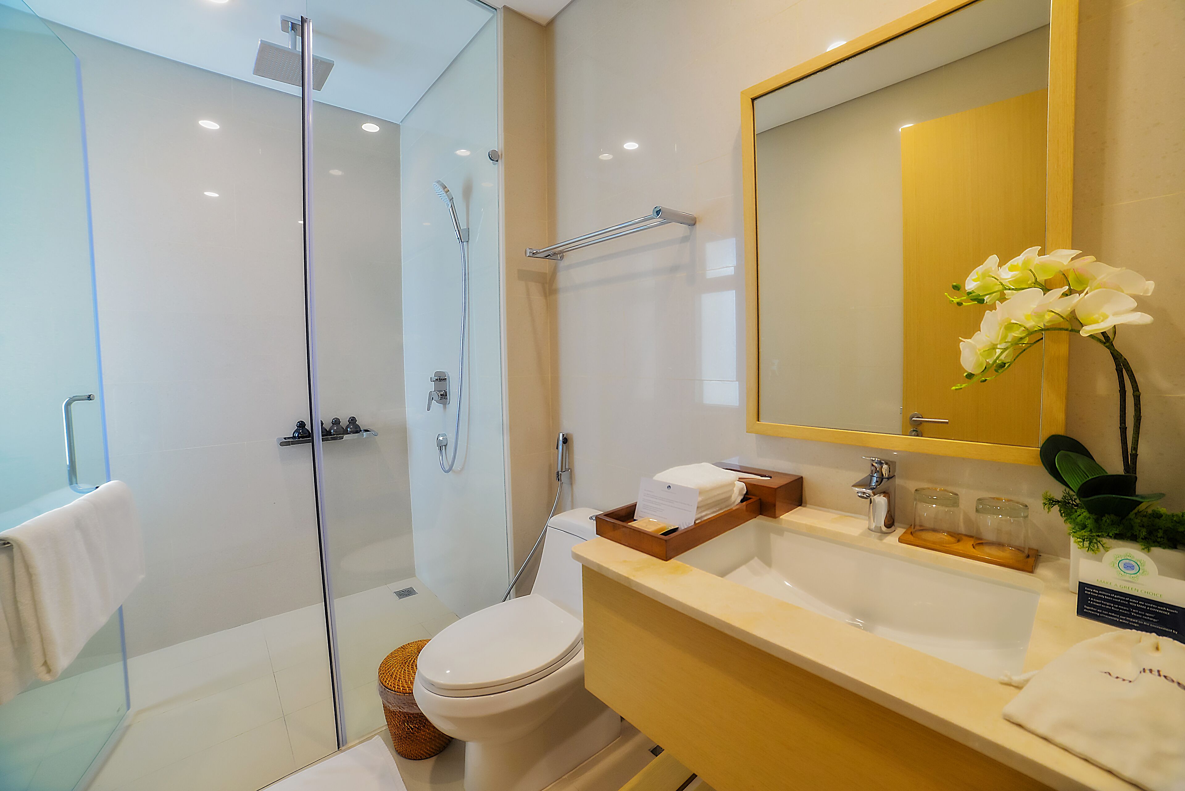 A modern bathroom with a glass-enclosed shower, a toilet, a sink with a mirror, and a small wicker basket.