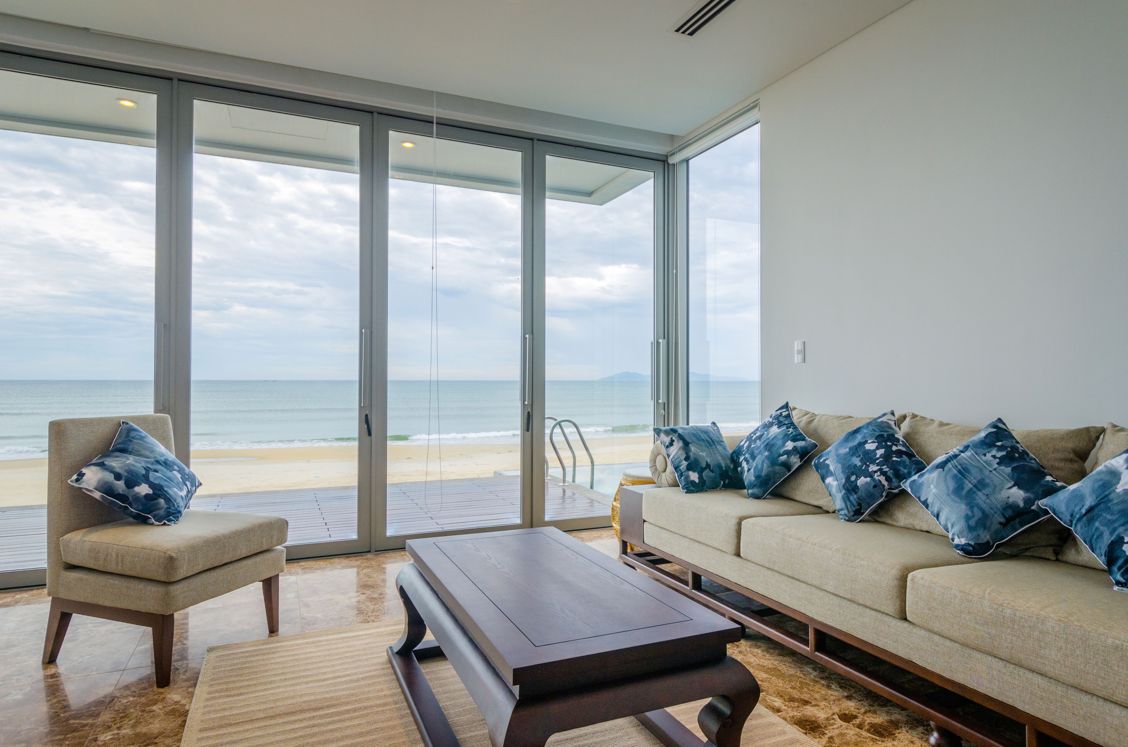 A modern living room with a large sliding glass door leading to a beach view.