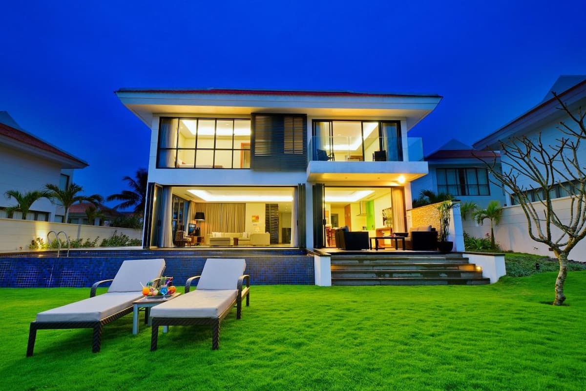 A modern two-story house with a well-maintained lawn, outdoor seating area, and a visible kitchen.