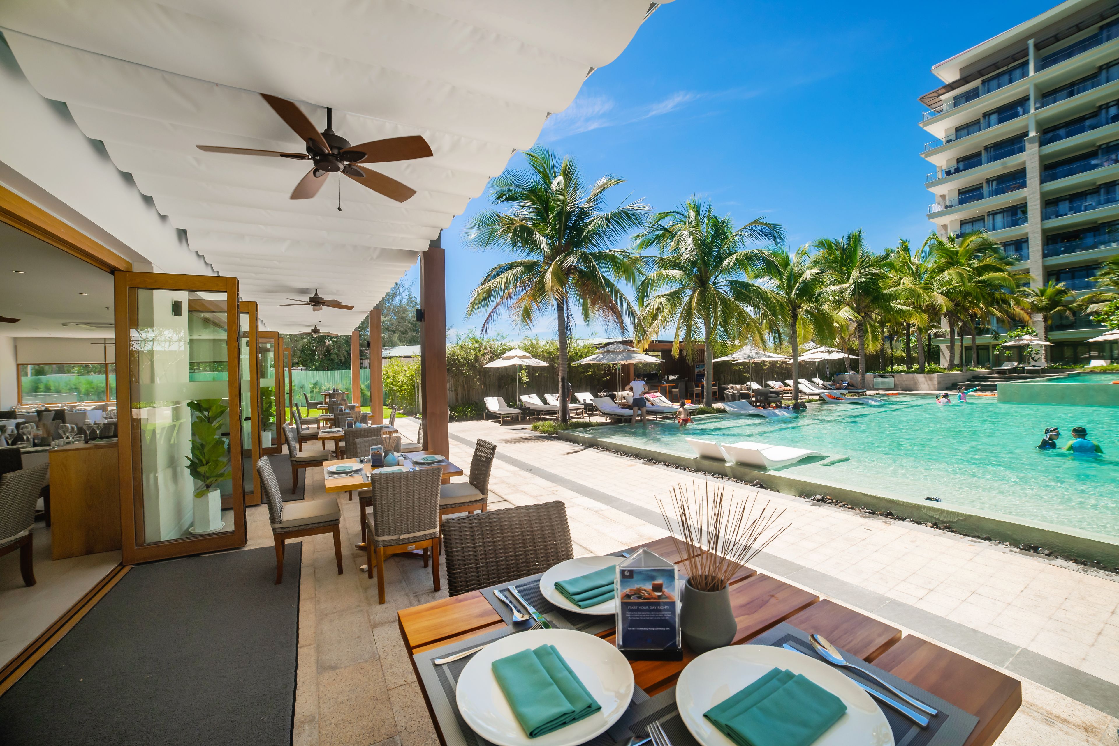 A hotel room with a dining area, a pool, and a view of palm trees.