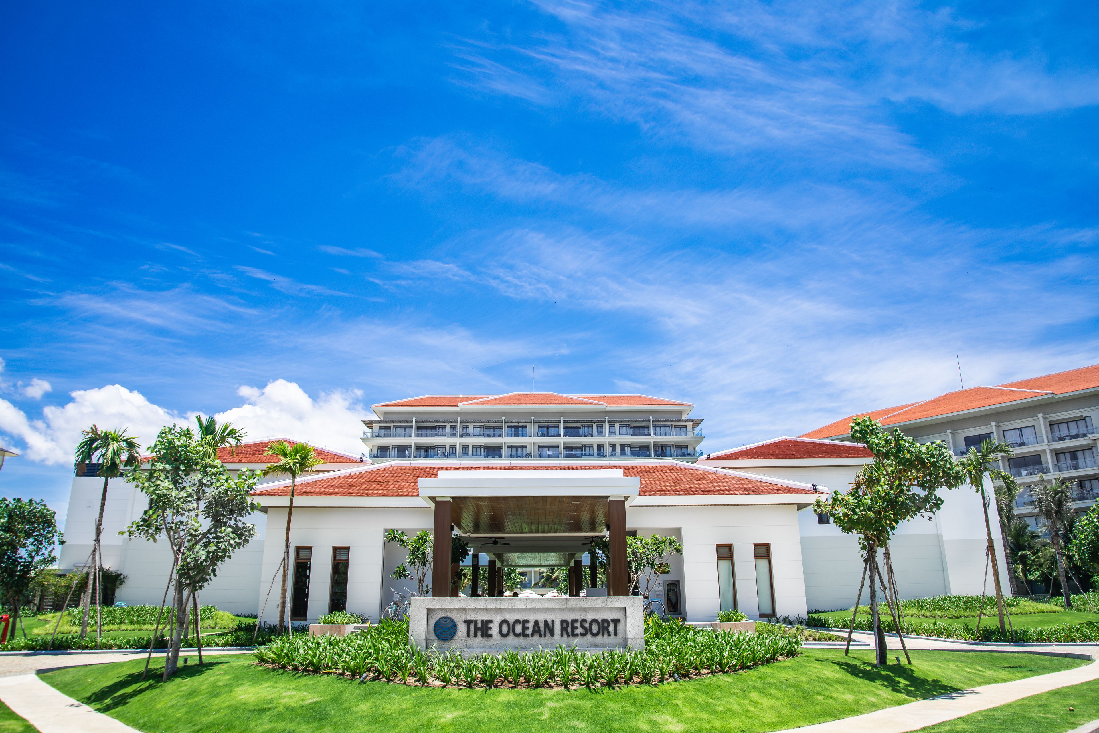 A hotel with a prominent entrance, a sign reading 'The Ocean Resort,' and a clear blue sky.