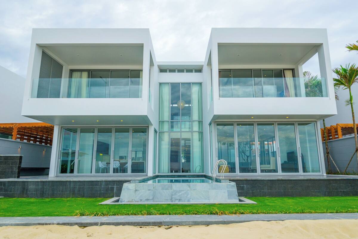 A modern two-story building with large glass windows, a swimming pool, and a well-maintained lawn.