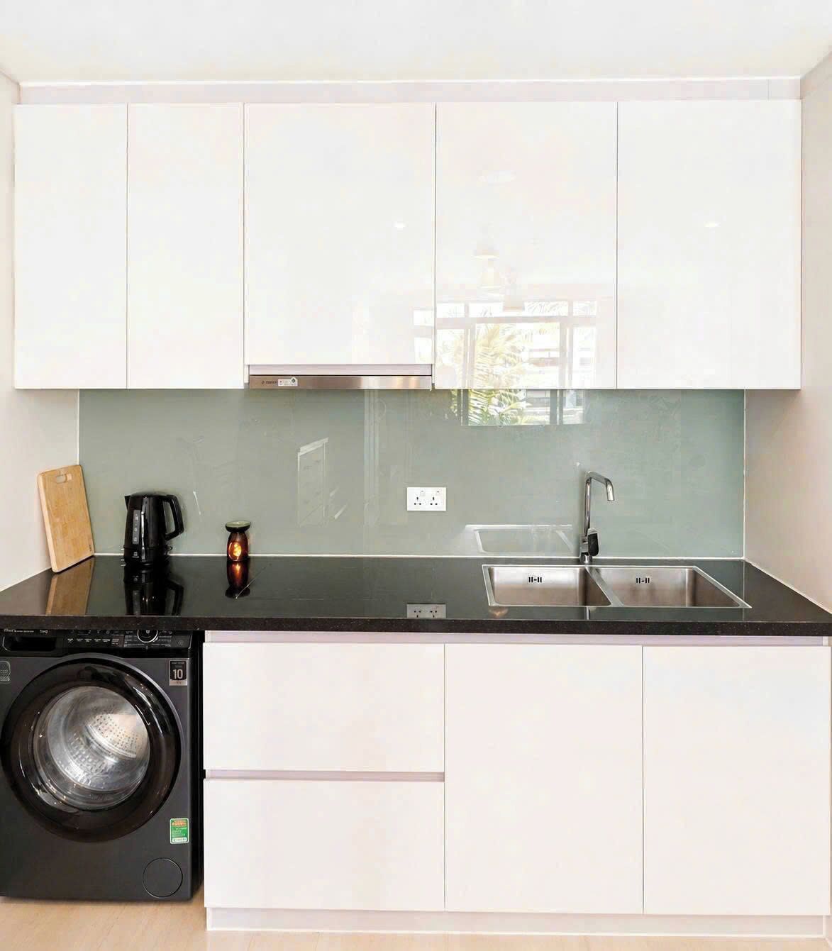 A compact kitchen with white cabinets, a stainless steel sink, a coffee maker, and a washing machine.