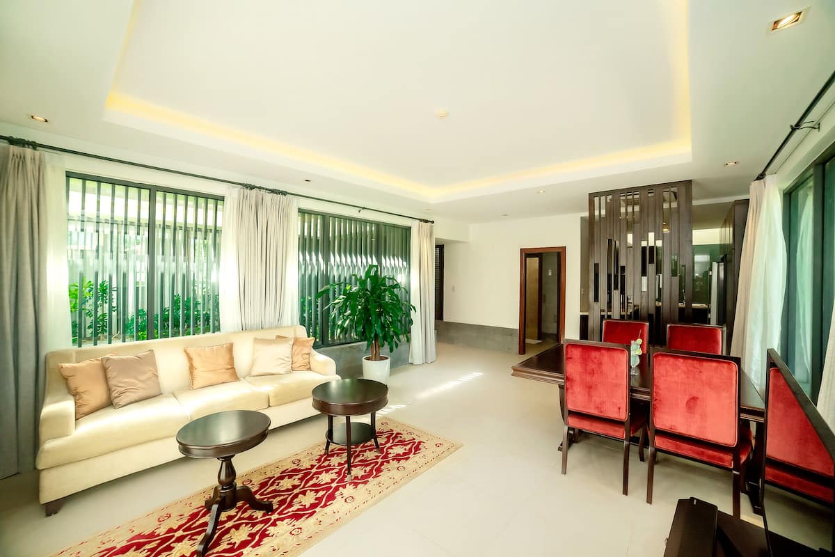 A modern living room with a sofa, a coffee table, and a dining area with red chairs.